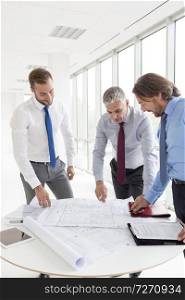 Businessmen discussing over blueprints at table in new office