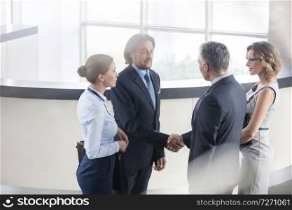Businessmen greeting while standing with colleagues at reception in office