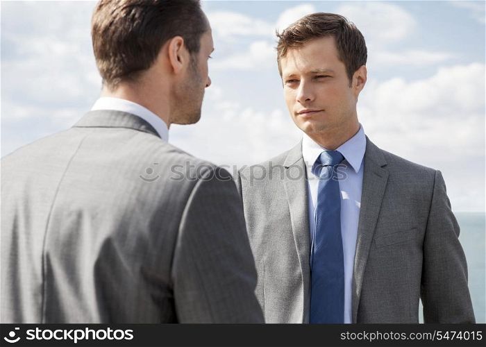 Businessmen looking at each other against sky