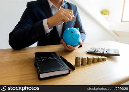 Businessmen putting coin In blue piggy Bank, saving money .finance concept .