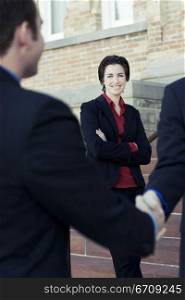 Businessmen shake hands while a business woman looks on their agreement