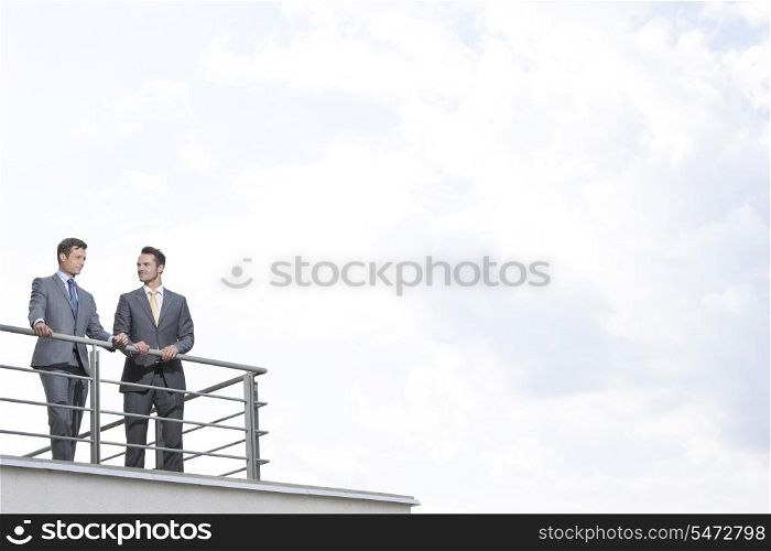 Businessmen standing at terrace railings against cloudy sky