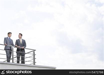 Businessmen standing at terrace railings against cloudy sky