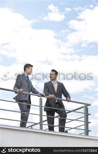 Businessmen standing at terrace railings against sky