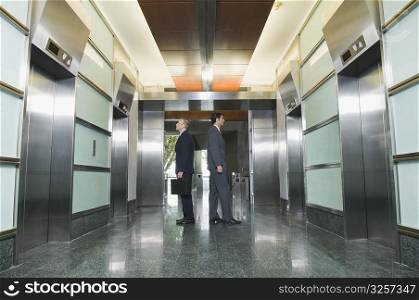 Businessmen standing back to back and waiting for elevators