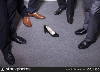 Businessmen standing in a circle around a woman&rsquo;s high heel, feet and legs only
