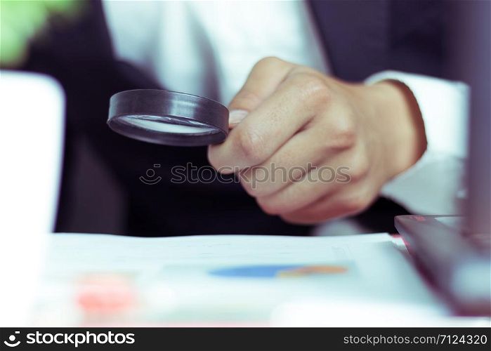 Businessmen use a magnifying glass to analyze the company&rsquo;s data and statistics from the chart.