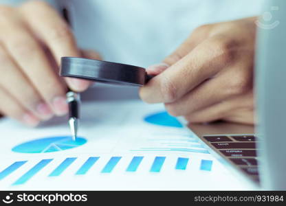 Businessmen use a magnifying glass to analyze the company's data and statistics from the chart.