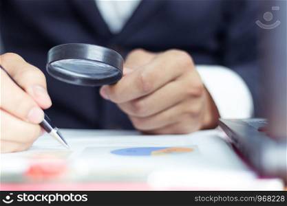 Businessmen use a magnifying glass to analyze the company's data and statistics from the chart.