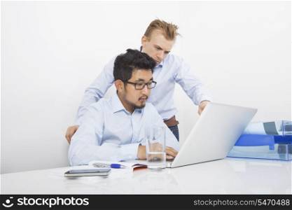 Businessmen using laptop together at desk in office