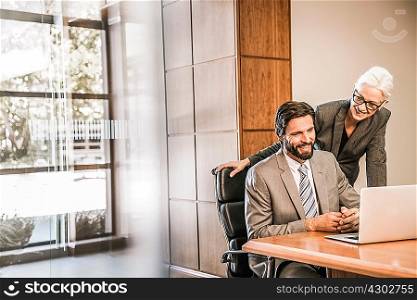 Businesspeople at desk looking at laptop smiling