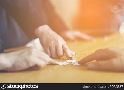 Businesspeople Hand Solving Jigsaw Puzzle On Wooden Desk, business concept