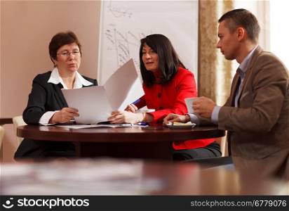 Businesspeople having a meeting over coffee sitting together at a table discussing a document, young man and two middle-aged women present