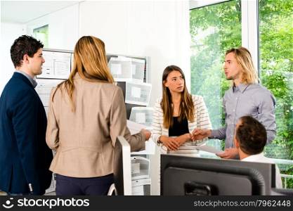 Businesspeople looking at bulletin board in office and discussing designs pinned at it. Mixed caucasian group rather casual, might be a startup comany or a creative agency.