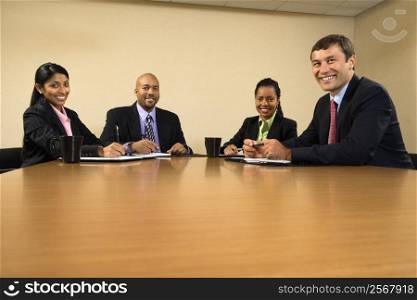 Businesspeople sitting at conference table smiling.