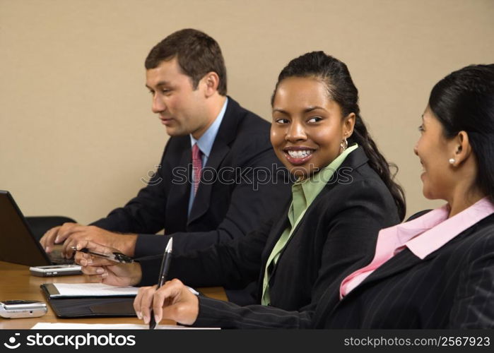 Businesspeople sitting at conference table talking and smiling.