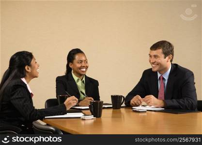 Businesspeople sitting at conference table talking and smiling.