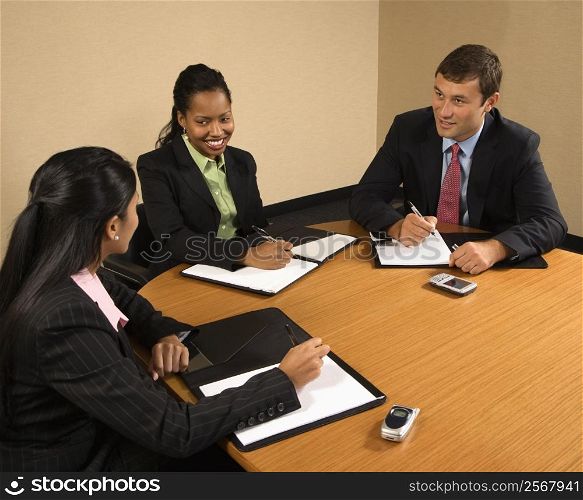 Businesspeople sitting at conference table talking and smiling.