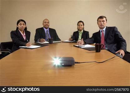 Businesspeople sitting at conference table watching LCD projector presentation.