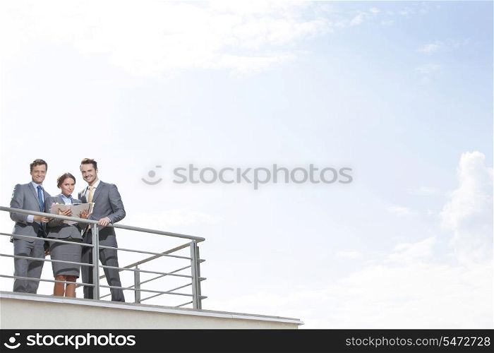 Businesspeople standing at terrace railings against sky