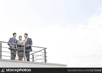 Businesspeople standing at terrace railings against sky