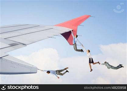 Businesspeople taking risk. Group of businesspeople hanging on edge of airplane wing