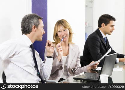 Businesspeople talking in meeting room. Businessman in the background using laptop