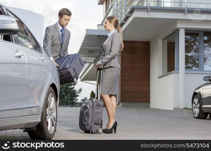 Businesspeople unloading luggage from car outside hotel