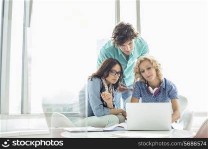 Businesspeople using laptop at table in creative office