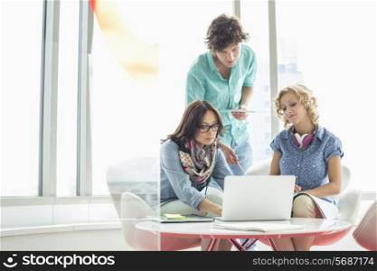 Businesspeople using laptop at table in creative office