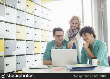 Businesspeople using laptop at table in locker room at creative office