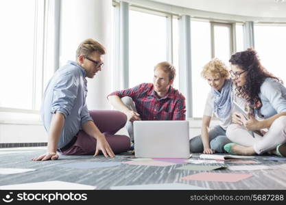 Businesspeople using laptop while sitting on floor at creative office