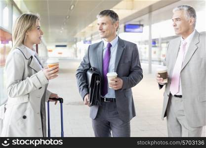 Businesspeople with coffee cups talking at railroad platform