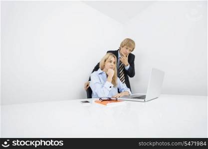 Businesspeople with hand on chin looking at laptop in office