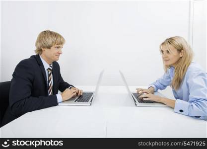 Businesspeople with laptops looking at each other in office
