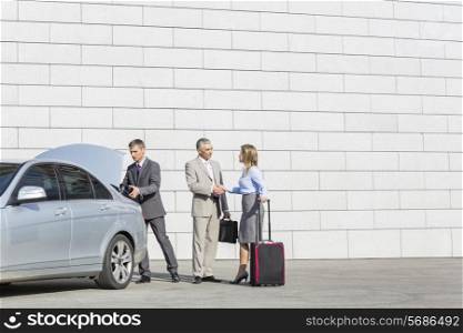 Businesspeople with luggage shaking hands outside car on street