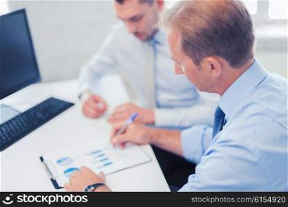 businesss and office concept - businessmen with notebook discussing graphs on meeting. businessmen with notebook on meeting