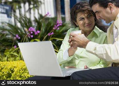 Businesswoman and a businessman sitting in front of a laptop and holding a cup of coffee