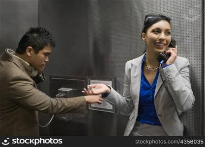 Businesswoman and a businessman talking on pay phones at an airport