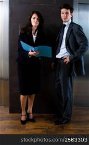 Businesswoman and businessman reviewing documents at office lobby in front of elevator. Dark background.