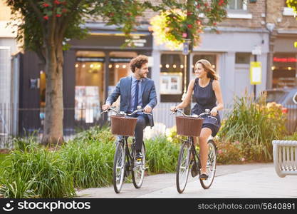 Businesswoman And Businessman Riding Bike Through City Park