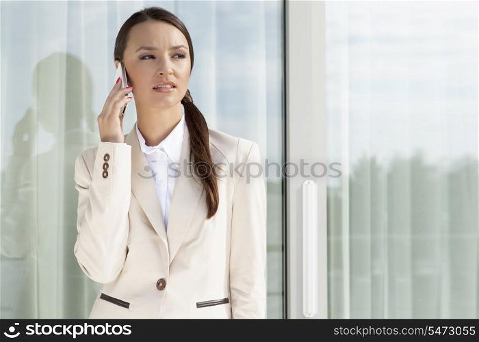 Businesswoman answering cell phone by glass door