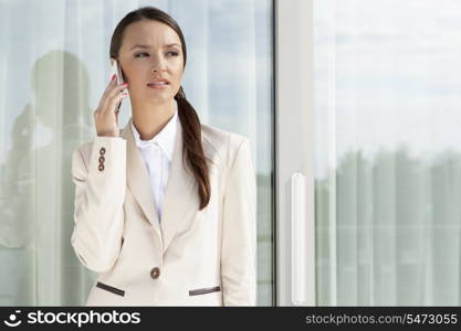 Businesswoman answering cell phone by glass door