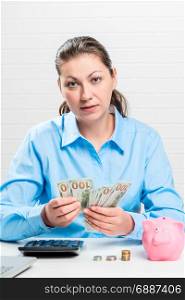 Businesswoman businesswoman counts dollars, near her a pink piggy bank