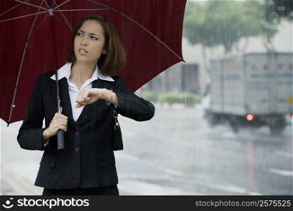 Businesswoman checking the time during rain