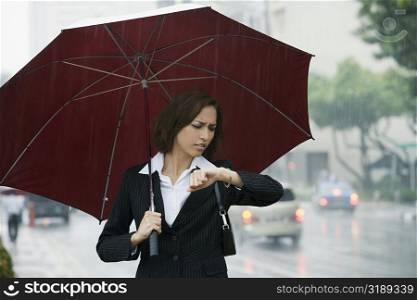Businesswoman checking the time during rain