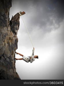 businesswoman climbing steep mountain hanging on rope