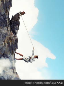 businesswoman climbing steep mountain hanging on rope