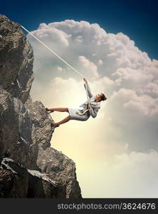 businesswoman climbing steep mountain hanging on rope