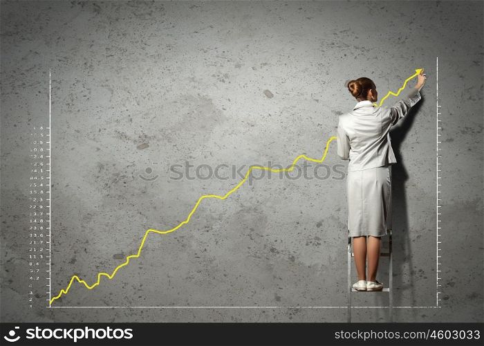 businesswoman drawing diagrams on wall. businesswoman standing on ladder drawing diagrams and graphs on wall